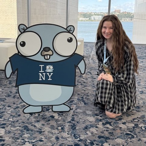 Bethany kneeling next to a Go gopher cutout at a conference
